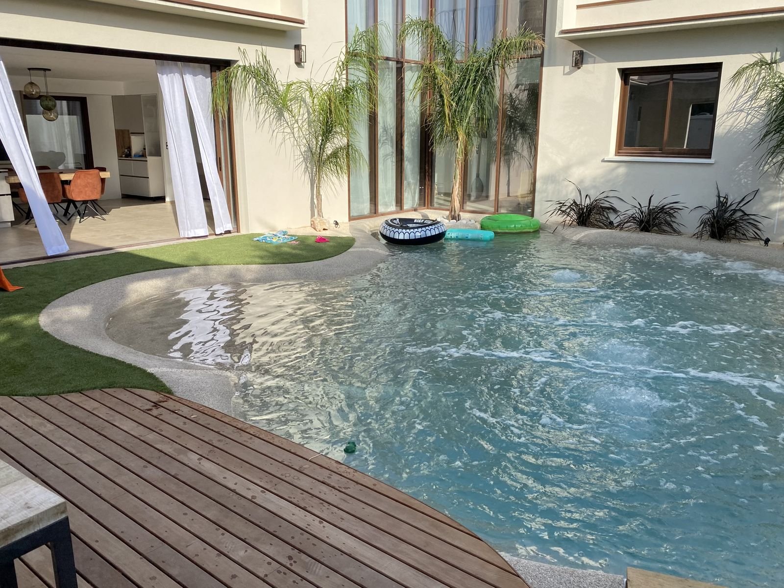 Piscine lagon bordée d'une terrasse en bois et de gazon synthétique